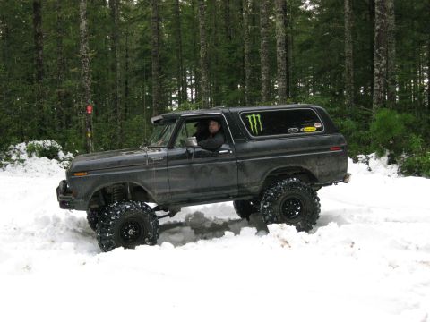 1979 Ford Bronco - A dark-colored SUV navigates a snowy forest road with its large off-road tires.