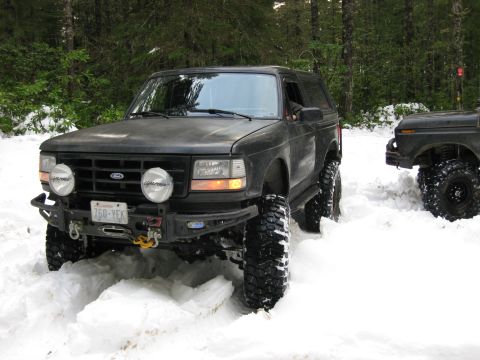 1979 Ford Bronco - Two off-road SUVs navigate a snowy forest trail during a winter excursion.