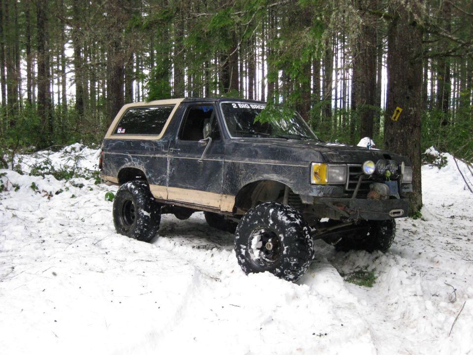 Ford Bronco with lifted suspension and large tires in snow, parked near trees