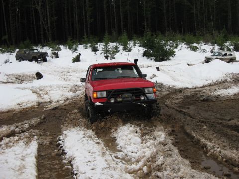1979 Ford Bronco - Several off-road vehicles navigate a snowy and muddy trail in a wooded area.