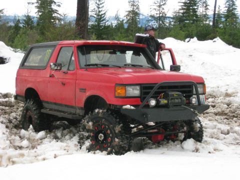 1979 Ford Bronco - A red off-road SUV is partially submerged in snow, with a person standing by the open driver's side door.