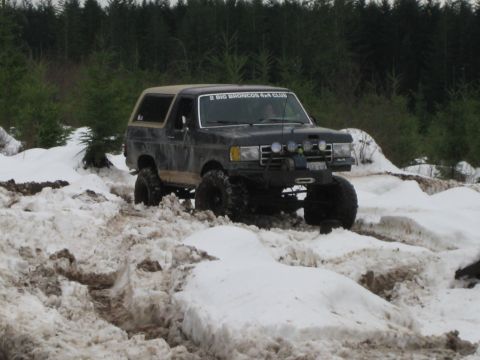 1979 Ford Bronco - A modified Ford Bronco navigates a snowy, muddy trail with a "2 BIG BRONCOS 4x4 CLUB" sticker on the windshield.