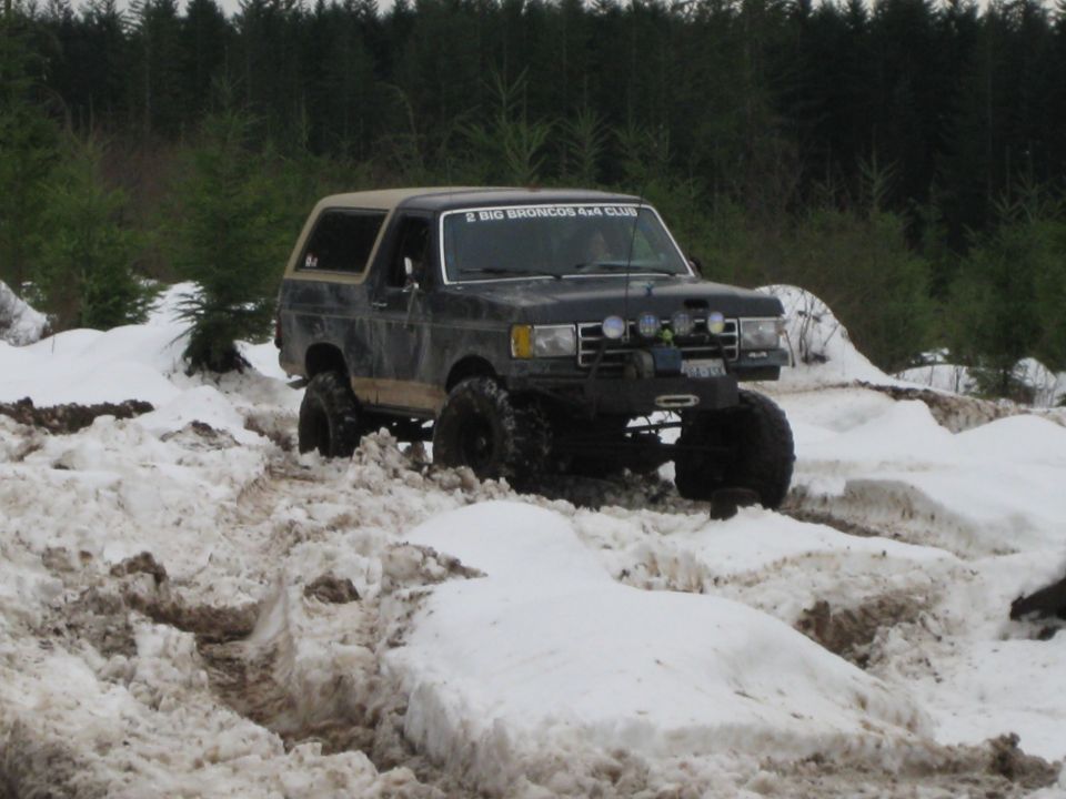 Black Ford Bronco with a tan top driving through snow, lifted suspension, aftermarket bumper with winch