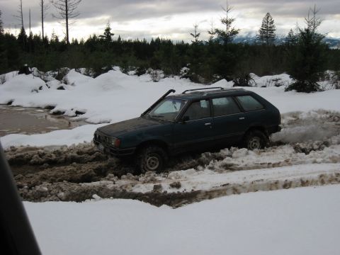 1979 Ford Bronco - A station wagon struggles through a muddy and snowy trail in a wooded area.