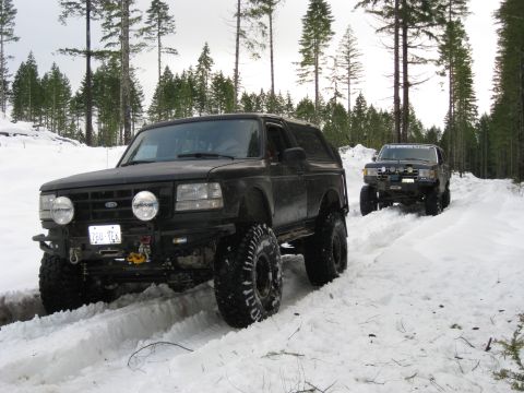 1979 Ford Bronco - Two modified Ford Broncos navigate a snowy forest road.