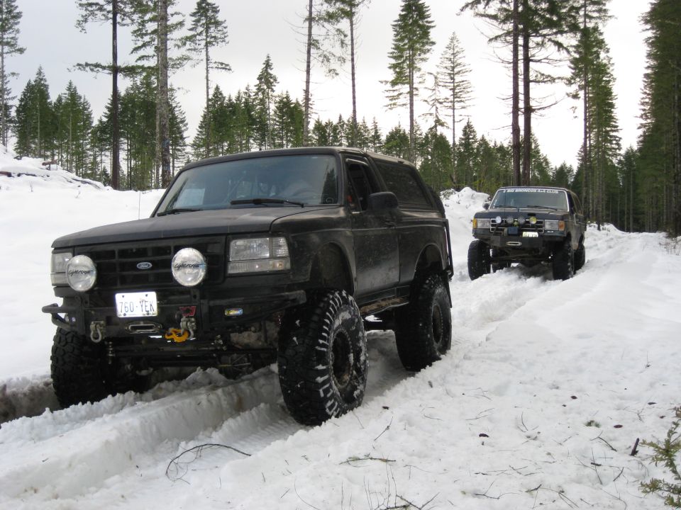 Black 1992 Ford Bronco with off-road tires driving in snow, front view