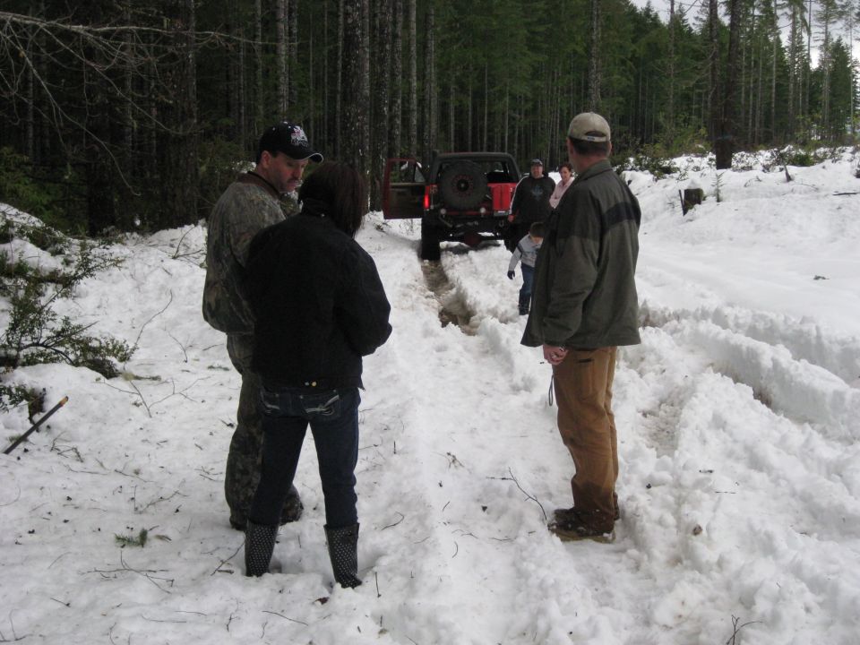 Red SUV stuck in snow, rear view. People gathered around