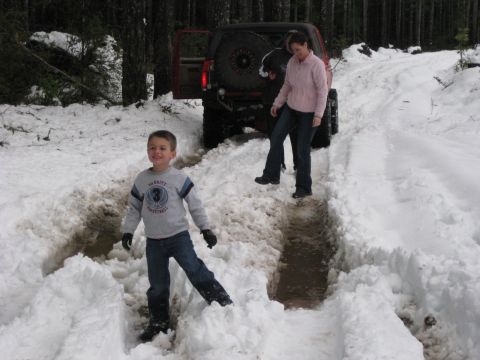 1979 Ford Bronco - A red SUV is stuck in the snow with two people nearby.