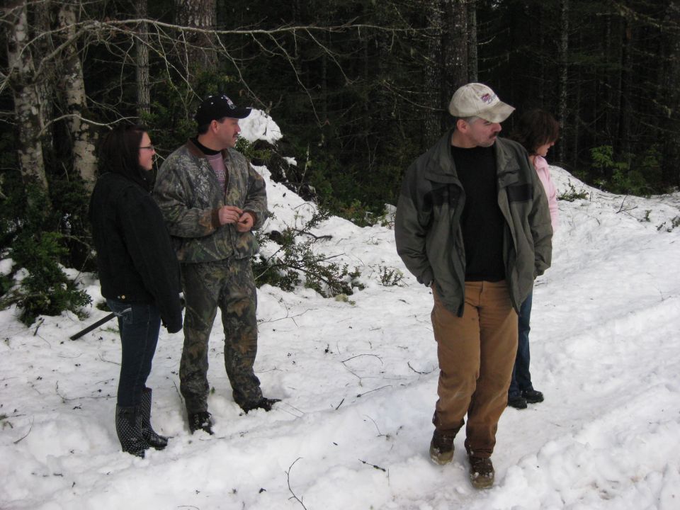 Four people stand in a snowy forest, looking off to the side