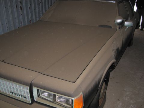 1991 Ford LTD Crown Victoria - A heavily dust-covered Chevrolet Caprice sits in storage, its grille clearly marked with the manufacturer's name.