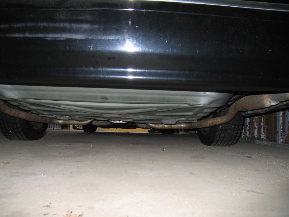 Underside view of a black car's exhaust system and tires