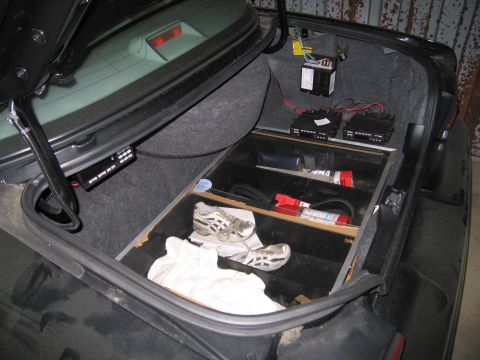 1991 Ford LTD Crown Victoria - The trunk of a car contains a custom-built compartment holding a pair of athletic shoes and various electronic devices.