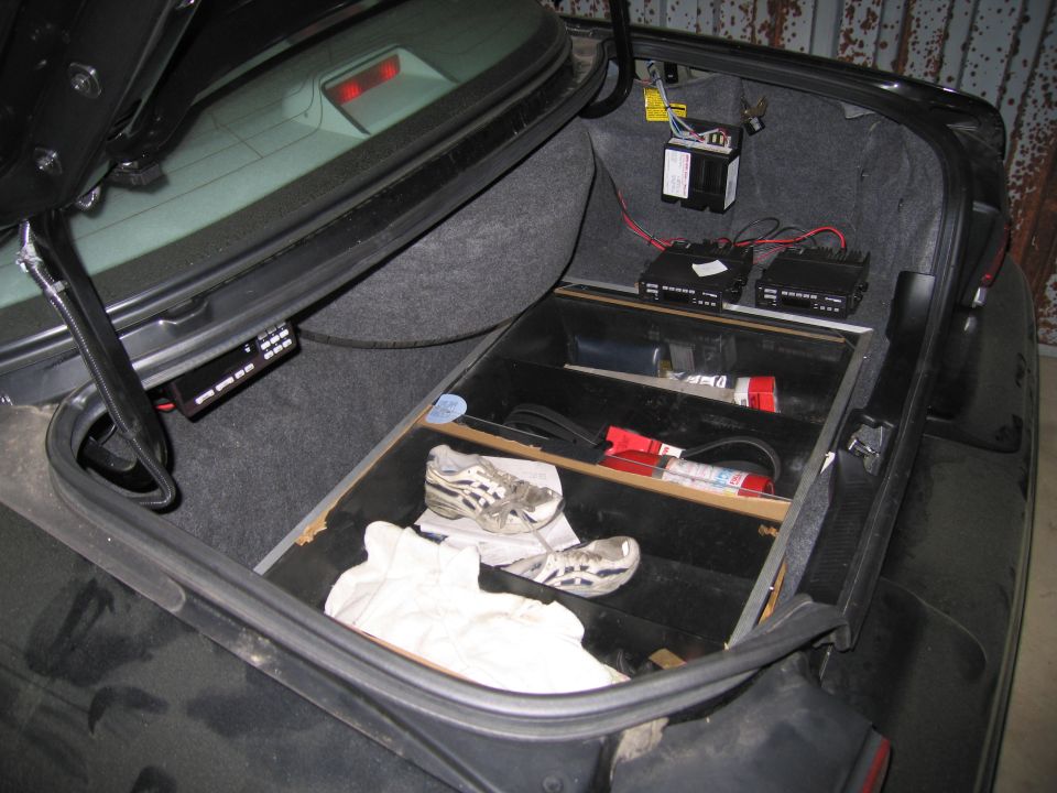 Car trunk open showing a custom storage compartment with shoes, gloves, and electronic equipment installed