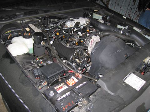 1991 Ford LTD Crown Victoria - The engine bay of a vehicle, showing the battery, fuse box, and engine components.