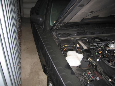 1991 Ford LTD Crown Victoria - The engine bay of a car is visible with the hood open, parked tightly between a wall and another object.