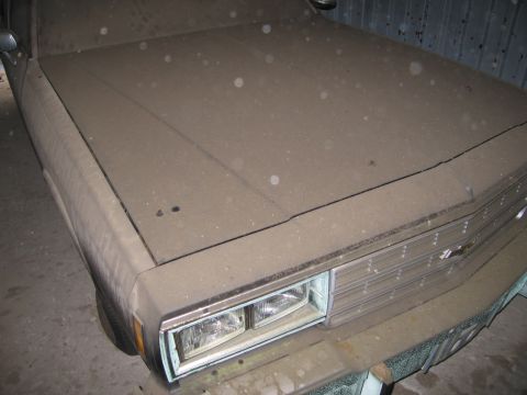 1991 Ford LTD Crown Victoria - A dusty car sits in storage, its front grille and headlights partially obscured by a thick layer of dust.
