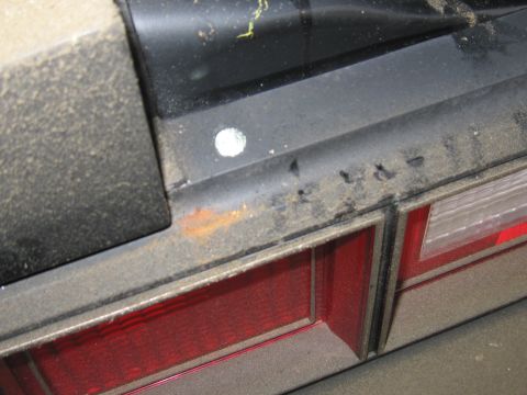 1991 Ford LTD Crown Victoria - Close-up of a dusty, dark-colored sedan's rear, revealing a red taillight and signs of rust on the trim.