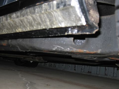1991 Ford LTD Crown Victoria - Close-up view of the lower door frame and undercarriage of a vehicle, showing signs of wear and rust.