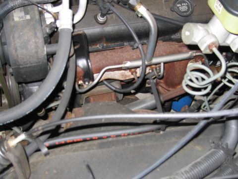 1991 Ford LTD Crown Victoria - This image shows various engine components, including hoses, wiring, and a rusty exhaust manifold, within a vehicle's engine bay.