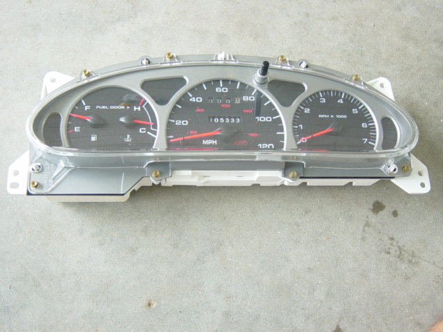 Removed vehicle instrument cluster with speedometer, tachometer and fuel/temp gauges on concrete