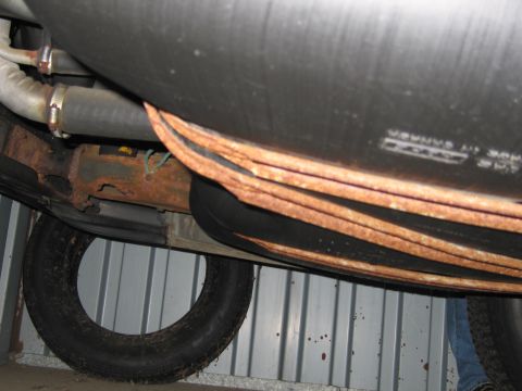 1991 Ford LTD Crown Victoria - The undercarriage of a vehicle reveals rusty leaf springs and a large fuel tank, with a spare tire visible below.
