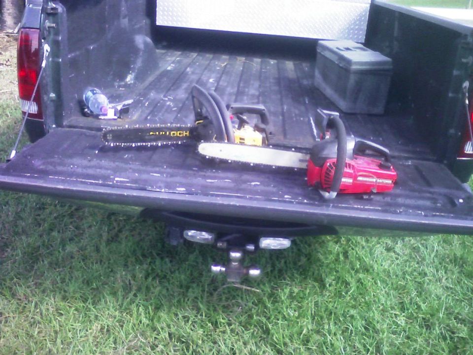 Two chainsaws resting on the tailgate of a dark-colored pickup truck