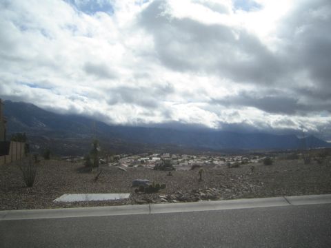 1968 Ford Mustang - A wide shot captures a residential area in a desert valley, with mountains looming under a dramatic sky.