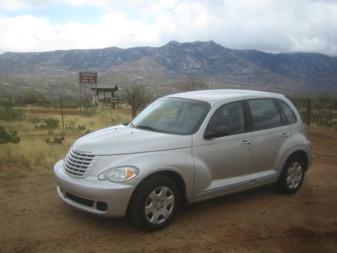 1968 Ford Mustang - A silver Chrysler PT Cruiser is parked outdoors with a mountainous backdrop and a sign in the distance.