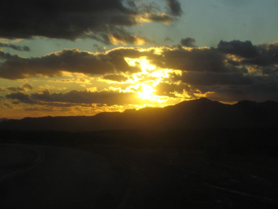 sun setting behind dark mountains, with clouds catching the light