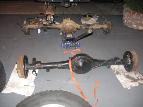 1989 Ford Bronco - Two vehicle axles are shown, one supported by a blue hydraulic jack, suggesting a repair or rebuild process.