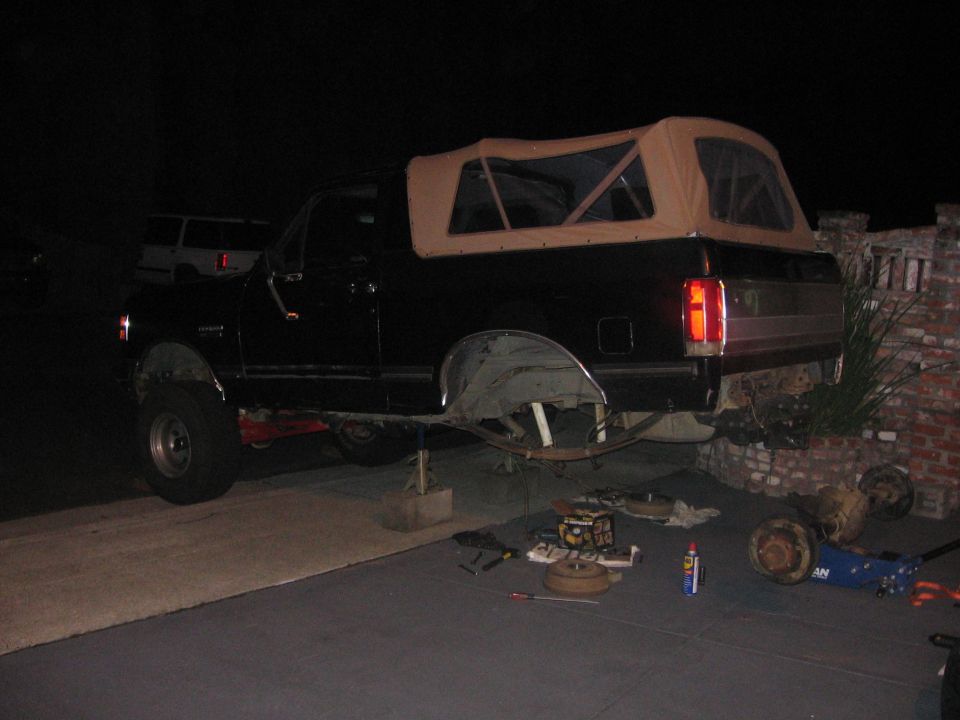 1989 Ford Bronco on jack stands with rear axle removed, parts scattered on the ground
