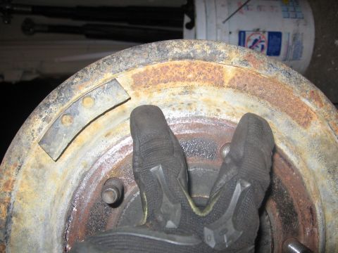 1989 Ford Bronco - Gloved hand on a rusty brake drum, showing two metal clips attached to the surface.