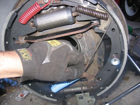 1989 Ford Bronco - A mechanic's gloved hand works on the brake drum assembly, replacing springs and shoes.