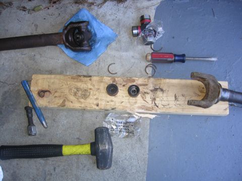 1989 Ford Bronco - Tools and disassembled driveshaft components are arranged on a wooden plank and concrete surface.