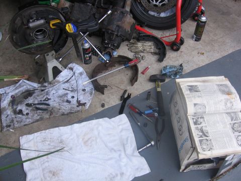 1989 Ford Bronco - Various automotive parts and tools are spread out on a concrete surface next to an open repair manual.