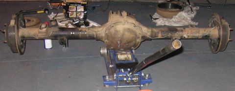 1989 Ford Bronco - A rear axle assembly is supported by a hydraulic jack on a concrete floor, with various tools and parts nearby.