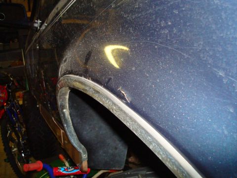 1995 Ford Bronco - The rear fender of a dusty, dark blue SUV is visible from the side, with a chrome trim piece around the wheel well.