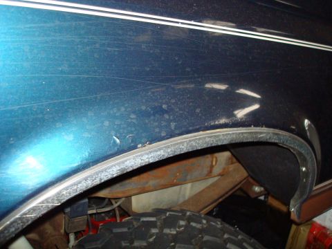 1995 Ford Bronco - Close-up of the rear wheel well on a 1995 Ford Bronco, showing signs of rust and wear.