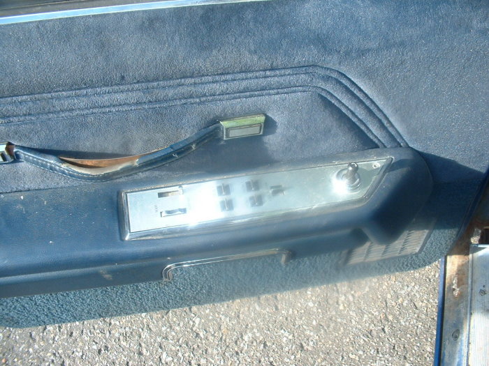 Blue fabric car door panel with power window controls and a torn pull handle