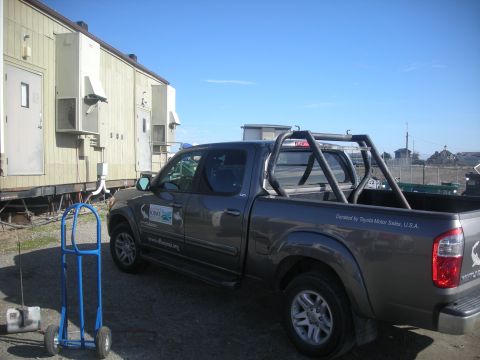 1991 Ford Bronco - Passenger-side rear three-quarter view of a gray Toyota Tundra SR5 double-cab pickup with a black tubular bed roll bar/light bar hoop, park…