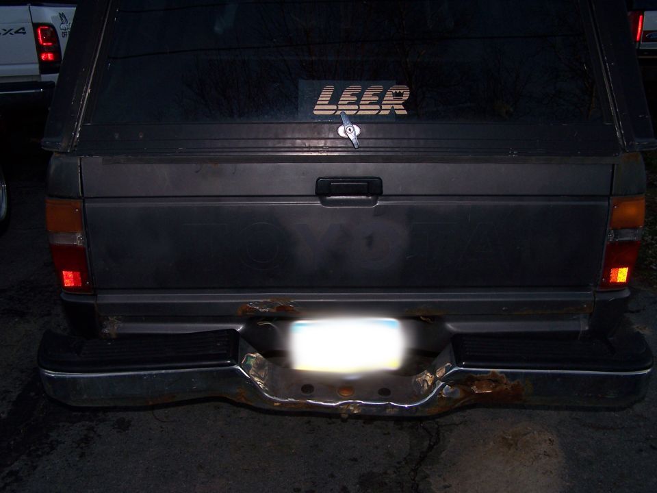Rear of a pickup truck with a Leer camper shell. Another white truck is partially visible to the left