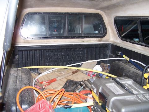 1988 Toyota Pickup/SR5 - The bed of a pickup truck is filled with various tools and items, including an extension cord, shovel, and a Coca-Cola can.