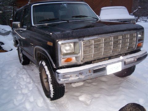 1986 Ford Bronco - A black Ford Bronco sits in the snow, its front grille and headlights partially covered by frost.