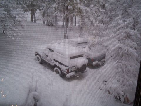 1986 Ford Bronco - Two SUVs are parked in a snowy landscape, partially buried under a thick blanket of snow.