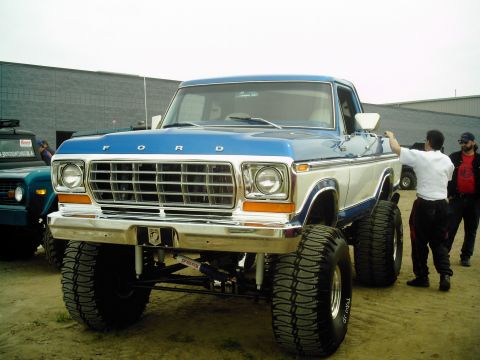 1995 Ford Bronco - This lifted Ford truck features a prominent grille and two-tone paint scheme, with another vehicle visible to the left.