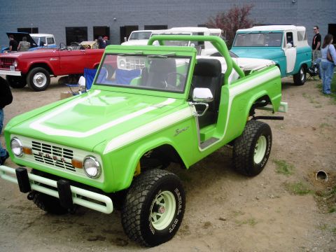1995 Ford Bronco - A lime green Ford Bronco with white racing stripes is parked outdoors, with other vehicles in the background.
