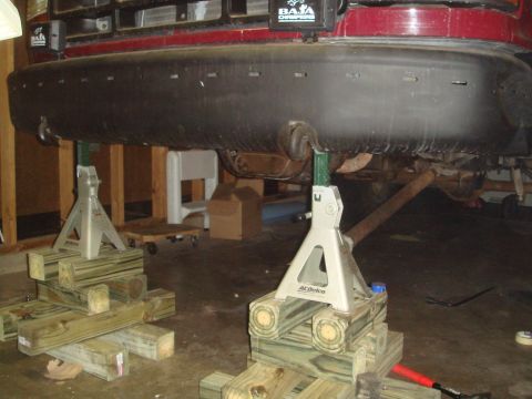 1992 Ford Bronco - The rear of a red 1992 Ford Bronco is elevated on jack stands, revealing its undercarriage and exhaust system.