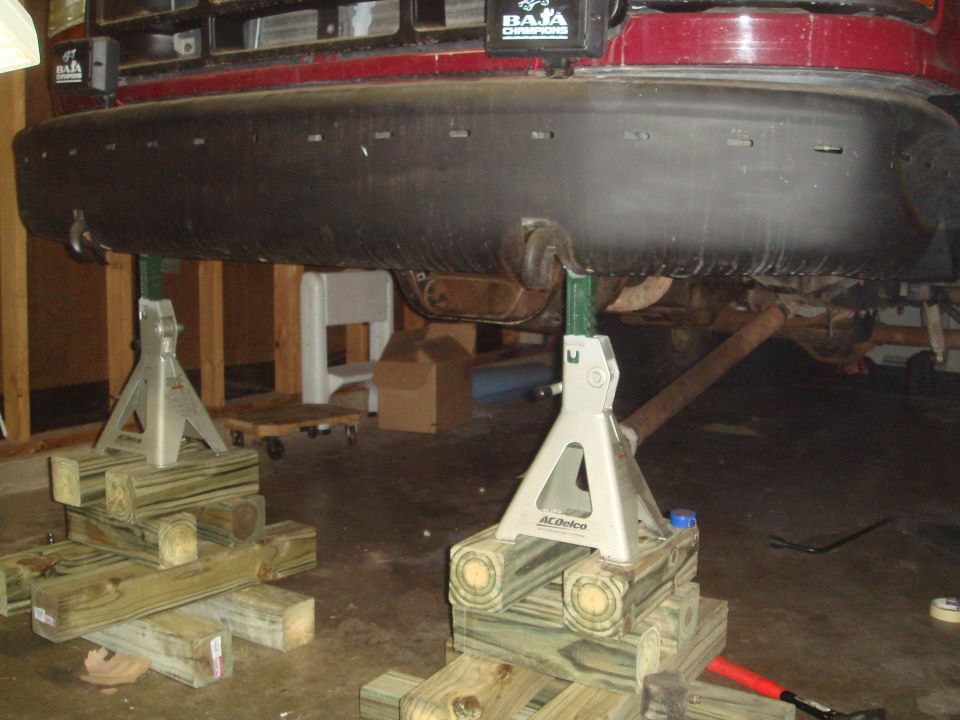 Red 1992 Ford Bronco rear bumper on jack stands, showing undercarriage and exhaust