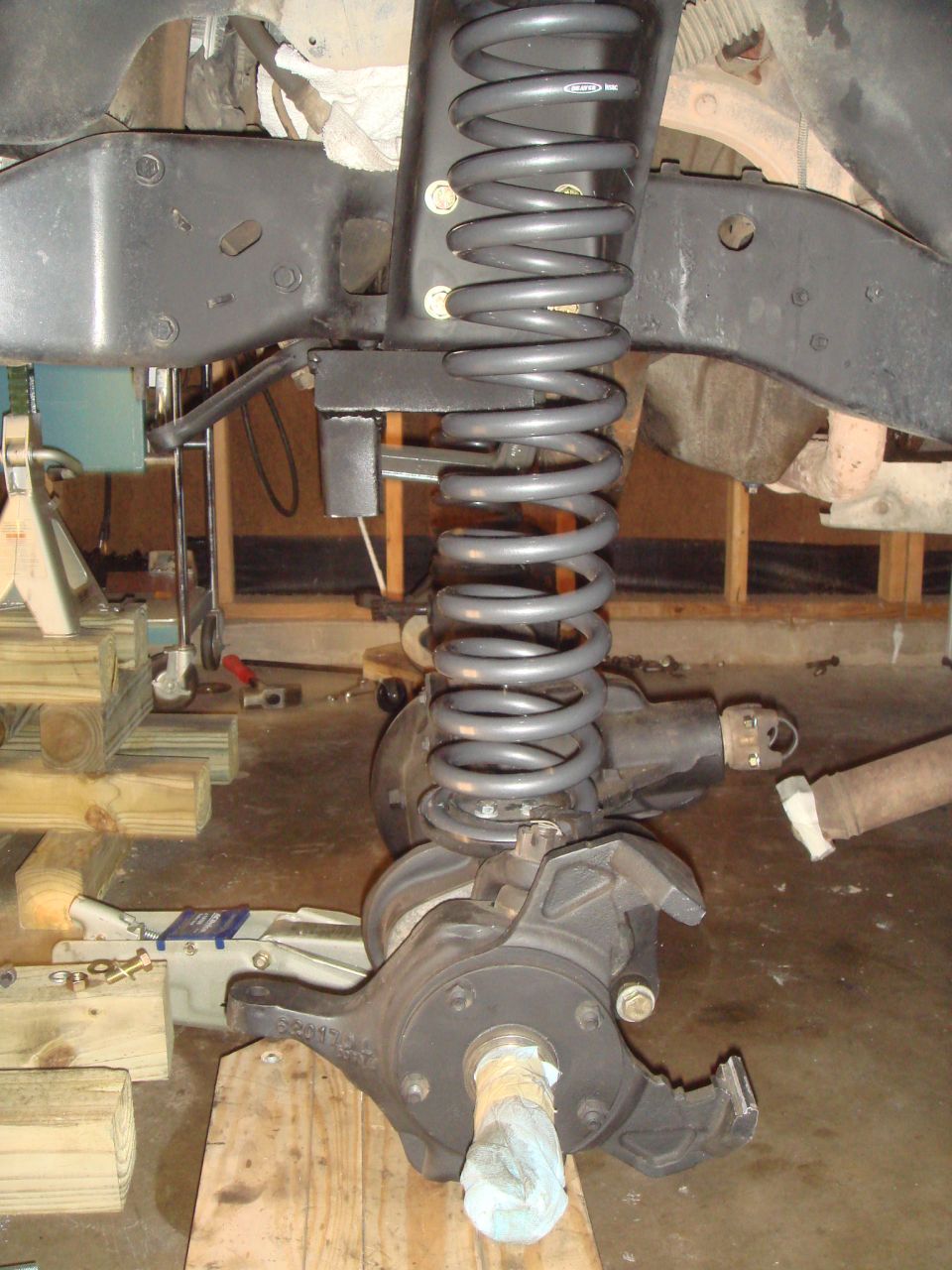 close-up of vehicle's front suspension and axle assembly, with a large coil spring and brake components visible