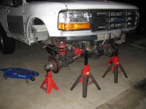 1996 Ford Bronco - Front suspension of a white truck, elevated on jack stands for maintenance.